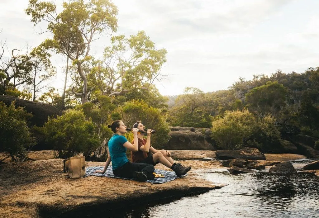 couple sitting by river drinking bottle of beer