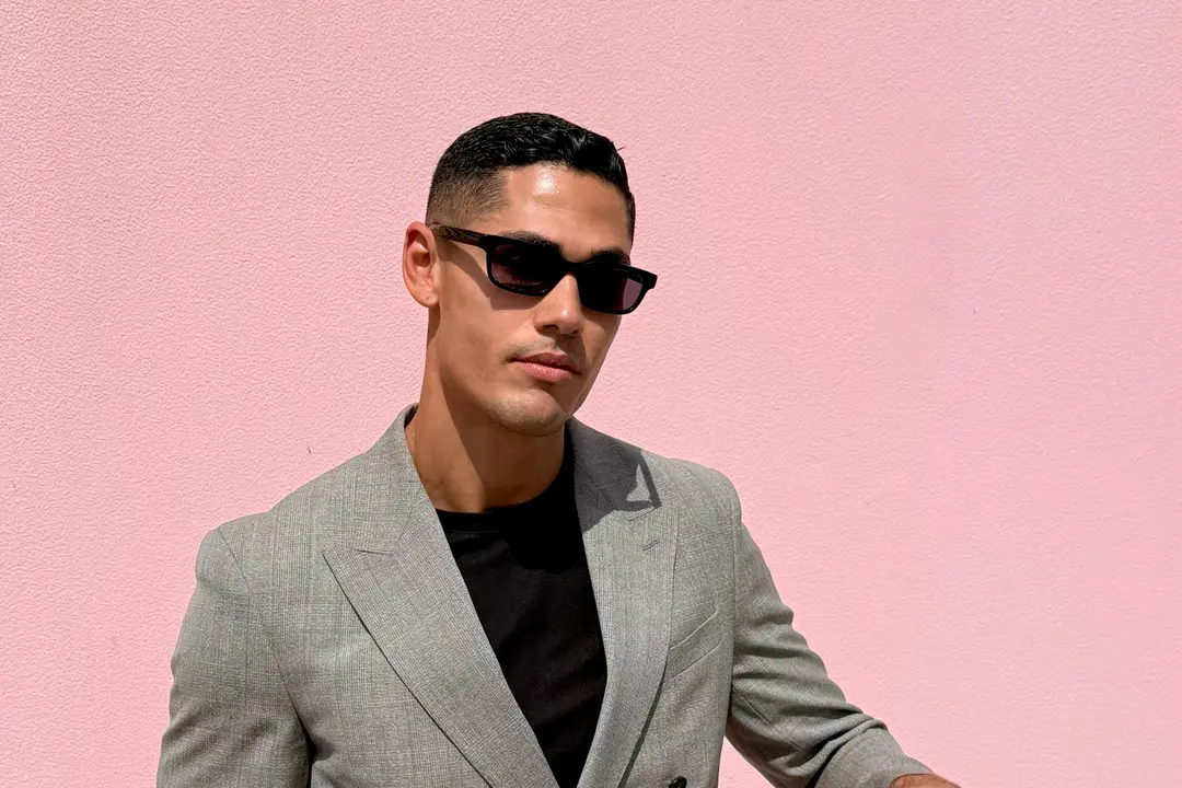 Creator @keelanbrissett in a grey double-breasted suit and dark sunglasses against a pink wall
