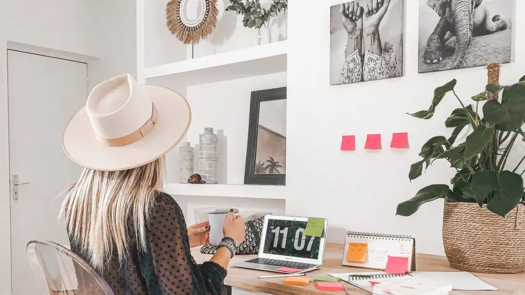 woman in hat at laptop with coffee in hand