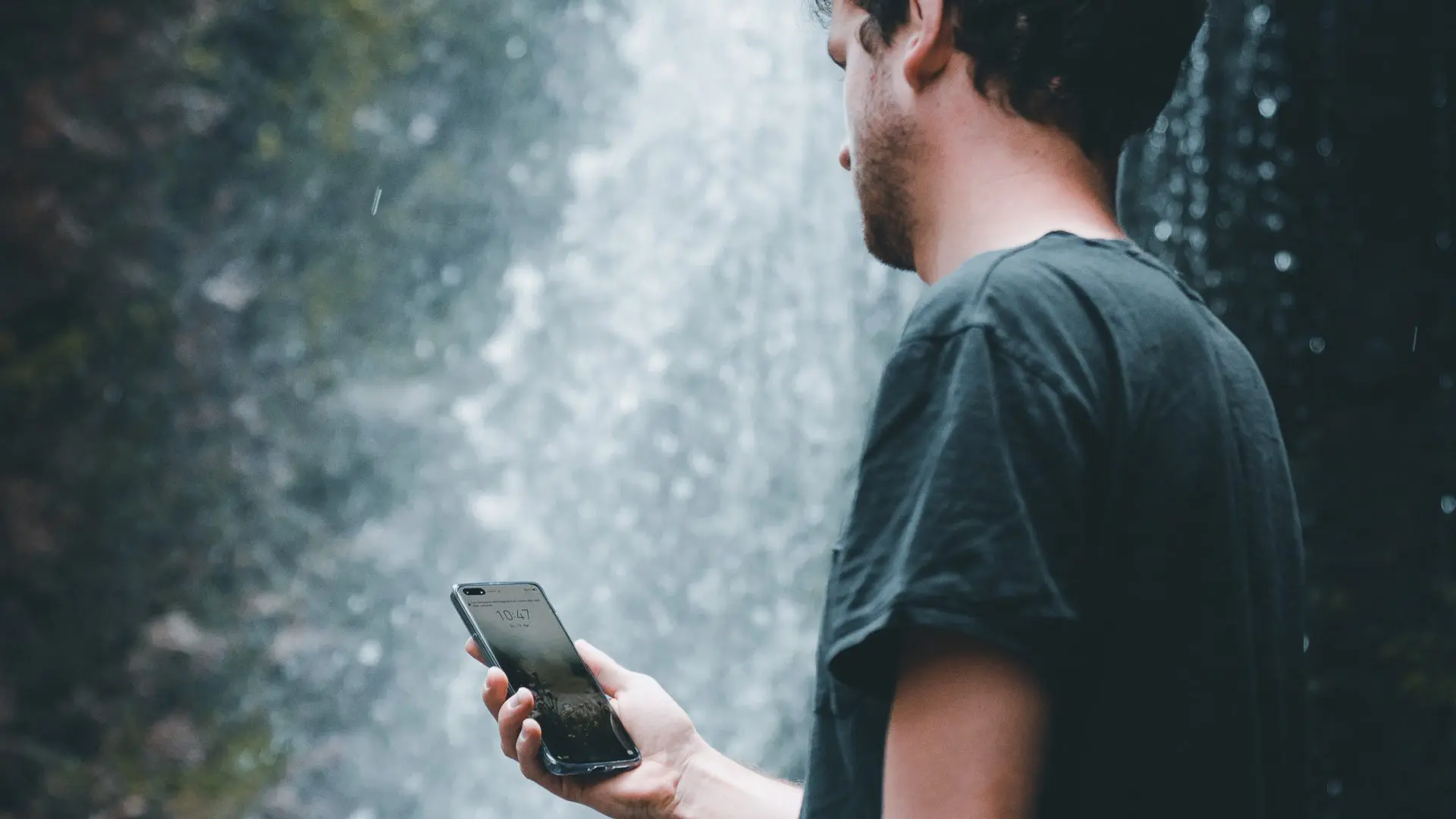 man with phone in front of waterfall