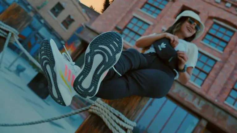 woman sitting on post wearing adidas trainers, black trousers, white top and bucket hat