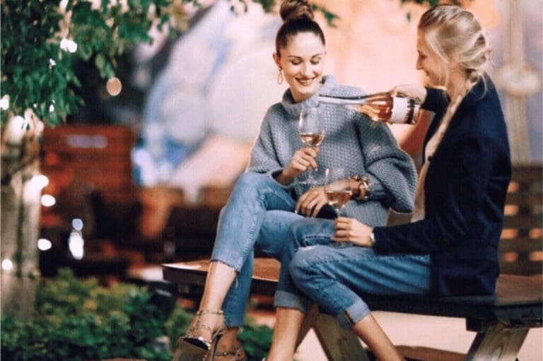 two women sitting on bench sharing wine