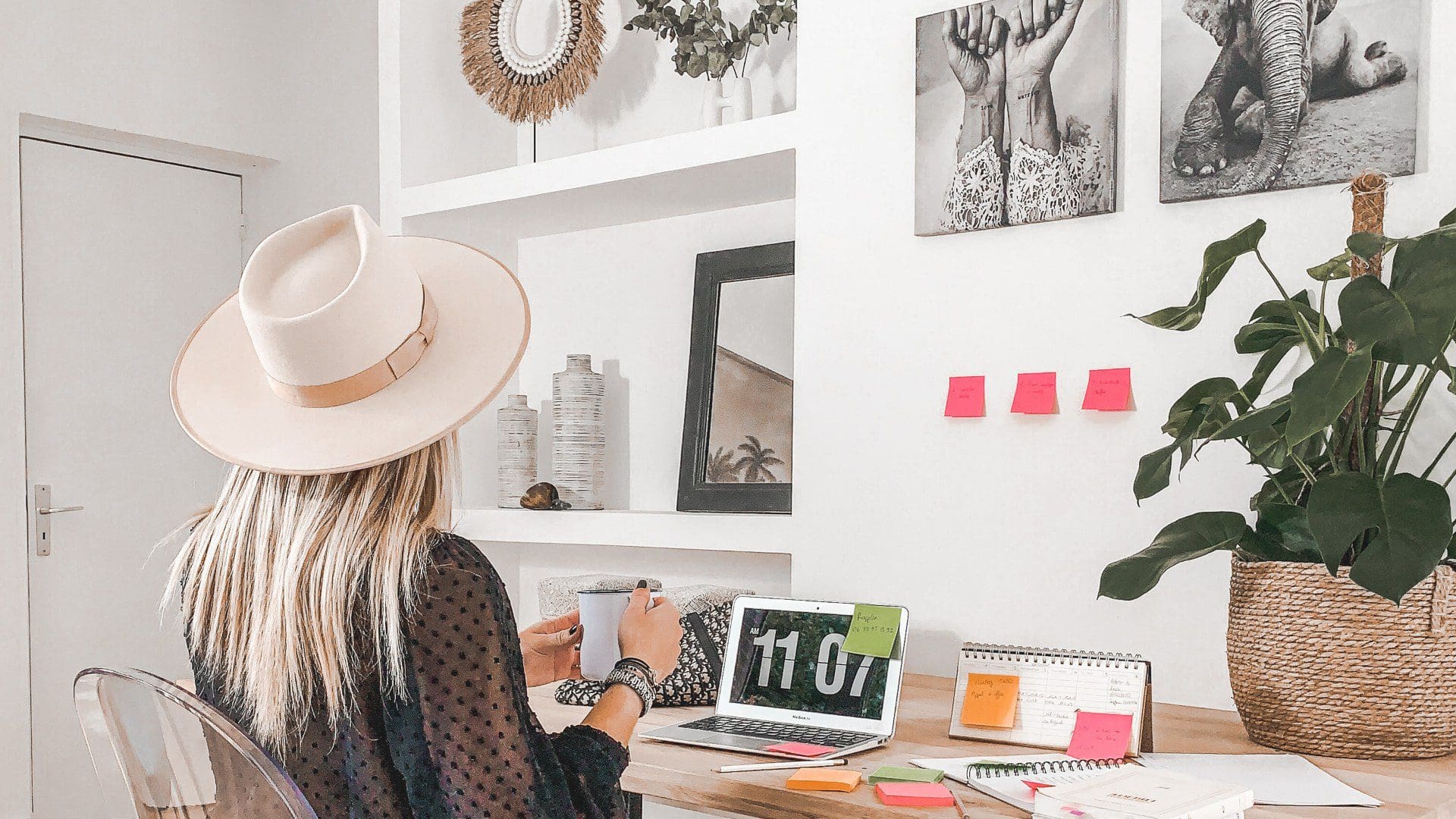 woman in hat at laptop with coffee in hand