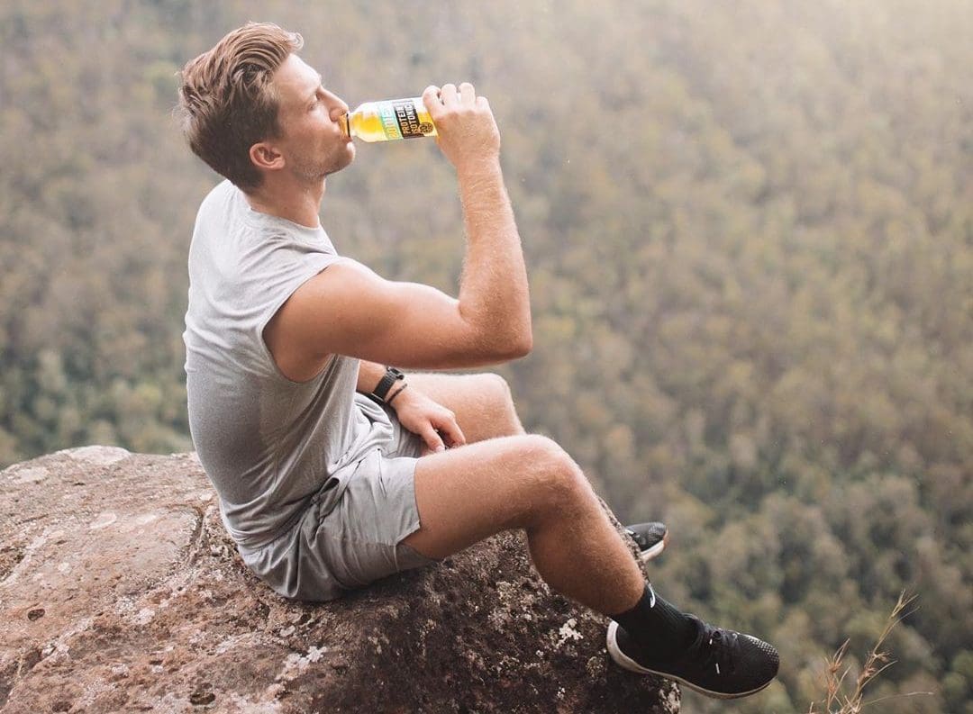 man on mountain edge drinking from bottle