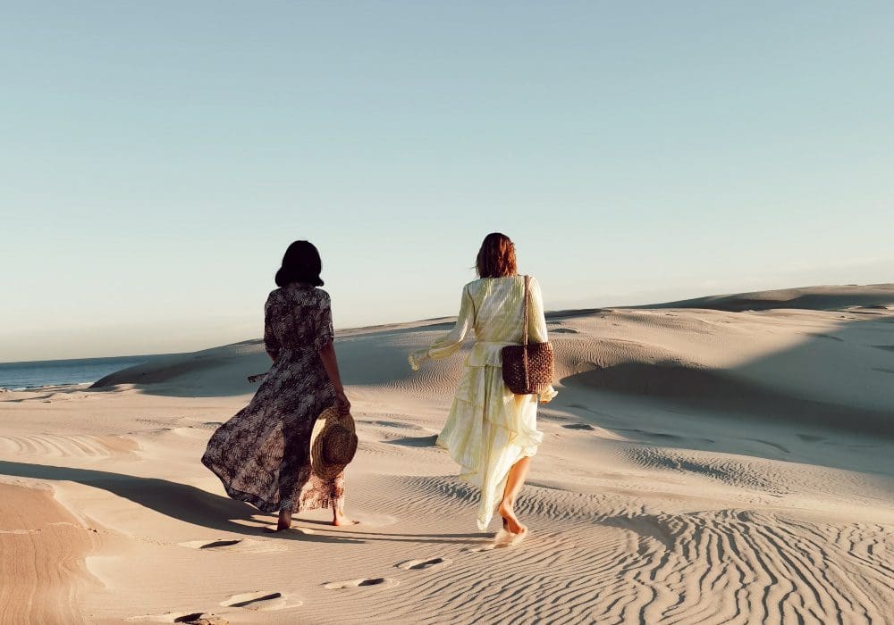 two women walking along sand