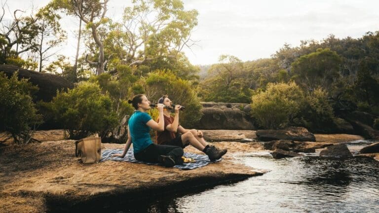 couple sitting by lake drinking bottled beer